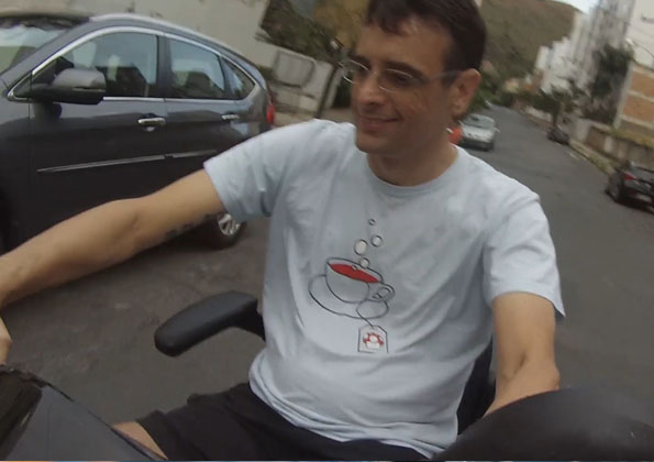 Um homem branco de óculos está sentado em um triciclo elétrico em uma rua de asfalto.